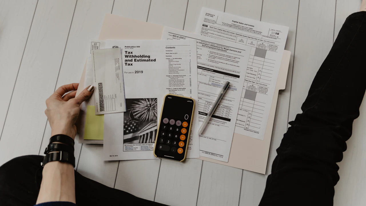 Documents administratifs, stylo et calculatrice affichée sur un téléphone